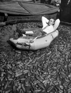 Dill Lamar Pickle reclining in a rubber boat in a vat of pickles for National Pickle Week.